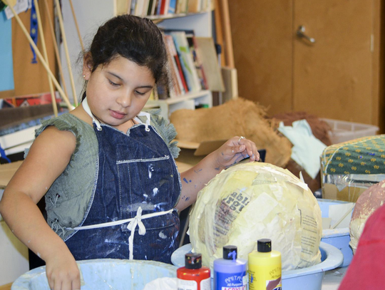 Sasha Moncada holds a fresh strip of paper wettedwith adhesive to begin shaping the facial features on the head of the paper-mache mermaid puppet.