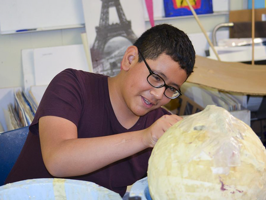 Elias Montelongo punctures the bottom of the papier-mâché mermaid head to pop the balloon inside that has been keeping the shape of the head in place while the paper dries.