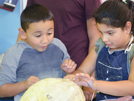 Abiel Montelongo watches as Sasha Moncada gives the popping of the balloon on the interior of the papier-mâché mermaid head a try.